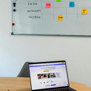 A modern office setup featuring a laptop and a whiteboard schedule for social media platforms.